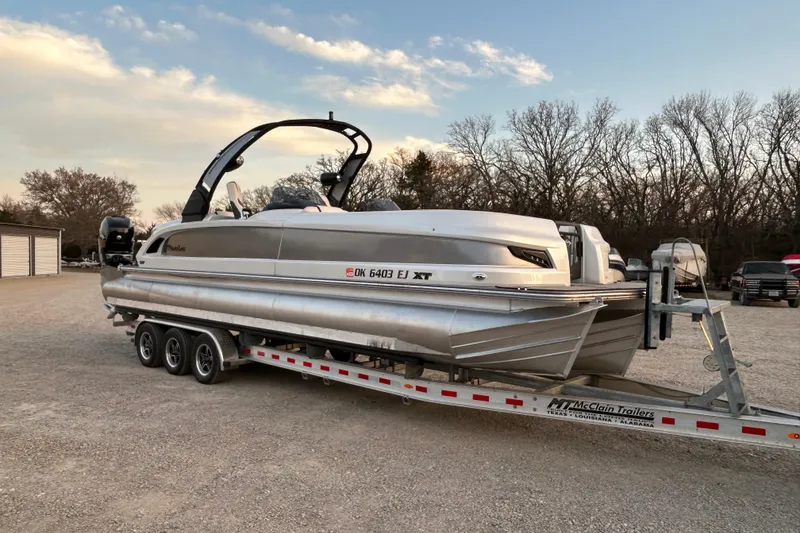 Slide: The Image of 2023 Manitou 270 pontoon boat on trailer, parked outdoors at sunset. - 1