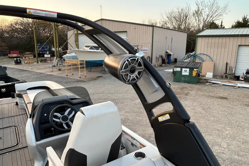 Slide: The Image of 2023 Manitou 270 boat interior with steering wheel and speaker, docked near storage buildings. - 21