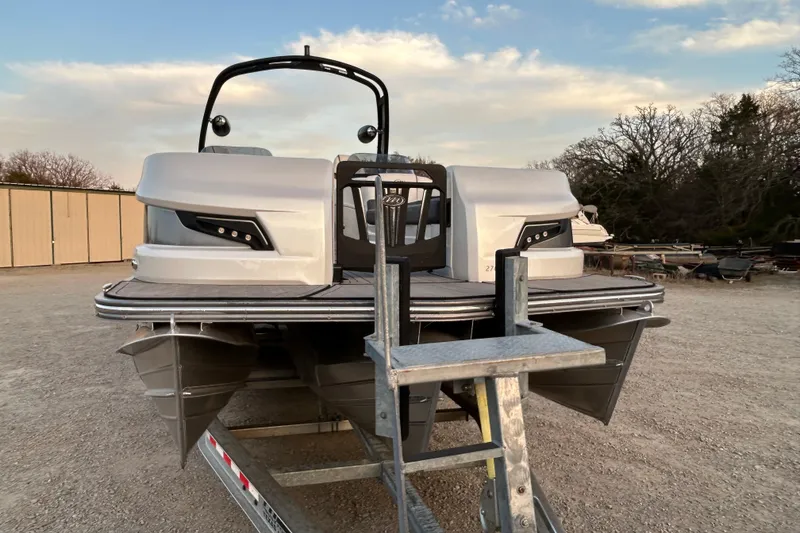 Slide: The Image of 2023 Manitou 270 pontoon boat on trailer, parked outdoors under a blue sky. - 3