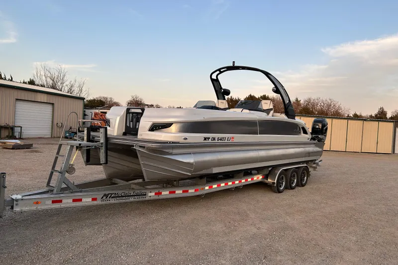 Slide: The Image of 2023 Manitou 270 pontoon boat on a trailer, parked outdoors near storage buildings. - 5