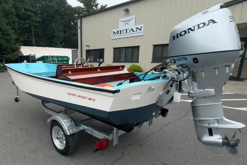 Slide: The Image of Manufacturer Provided Image: 2026 Metan Super Sport 13 boat with Honda outboard motor, parked outside Metan Marine Restoration. - 2