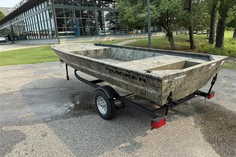 Slide: The Image of 2026 Tracker Grizzly 1648 Utility boat on trailer, parked outdoors near trees and building. - 2