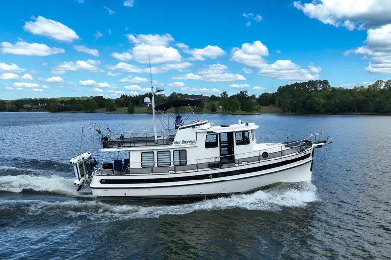 Slide: The Image of 2000 Nordic Tug 42 Flybridge cruising on a scenic lake under a clear blue sky. - 2