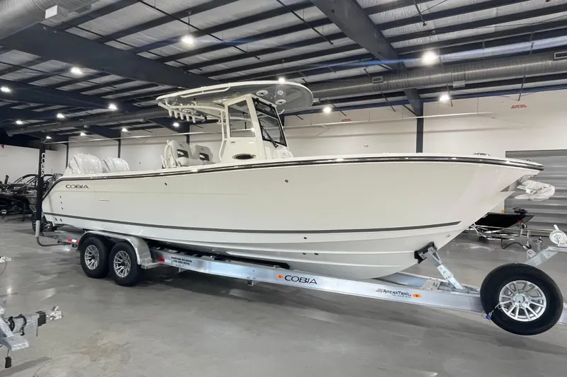 The Image of 2026 Cobia 285 Open Center Console boat on trailer in showroom. - 0