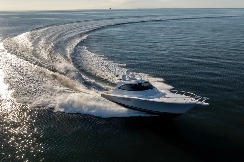 Slide: The Image of 2022 Viking 54 Sport Coupe yacht cruising on open water, creating dynamic wake patterns. - 11