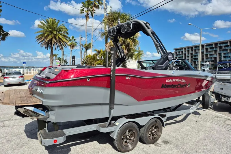 Slide: The Image of 2022 MasterCraft X24 boat on trailer, vibrant red and gray, parked near palm trees. - 3