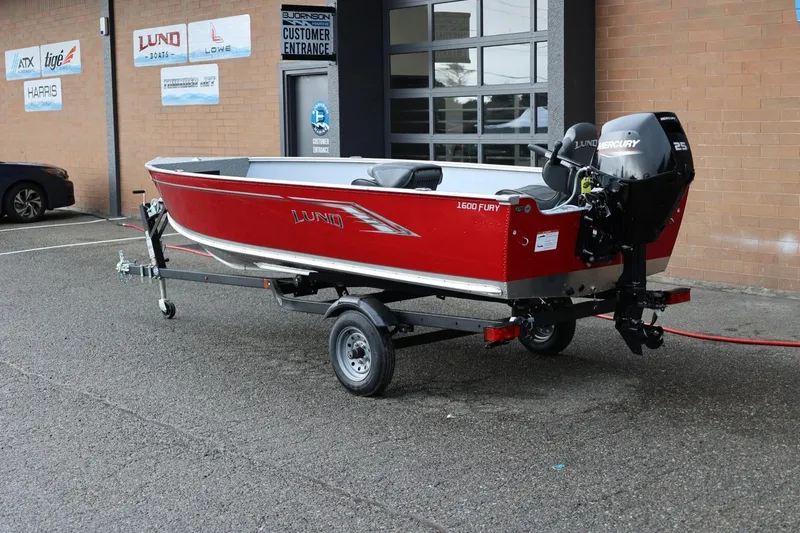 Slide: The Image of 2026 Lund 1600 Fury Tiller boat on trailer, parked outside dealership. - 3