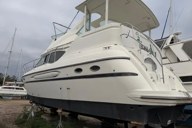 Slide: The Image of 2000 Maxum 4100 SCA yacht on land, white exterior, docked among other boats. - 10