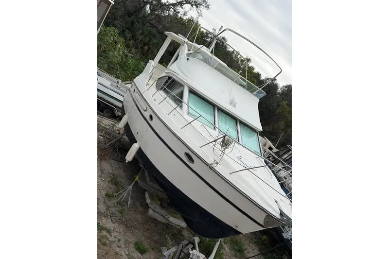 Slide: The Image of 2000 Maxum 4100 SCA yacht on land, surrounded by trees and other boats. - 4