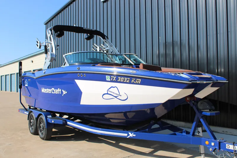 Slide: The Image of 2021 MasterCraft XStar boat in blue on a trailer, parked outside a warehouse. - 2