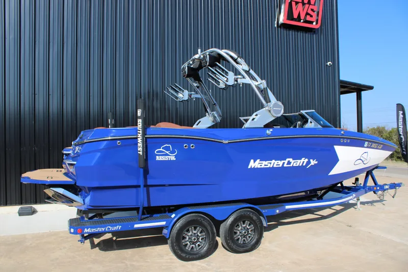 Slide: The Image of 2021 MasterCraft XStar boat in vibrant blue on a trailer, parked outdoors. - 3