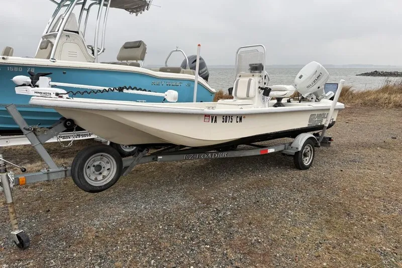The Image of 2006 Carolina Skiff JV17 boat on trailer by the shore, overcast sky. - 0