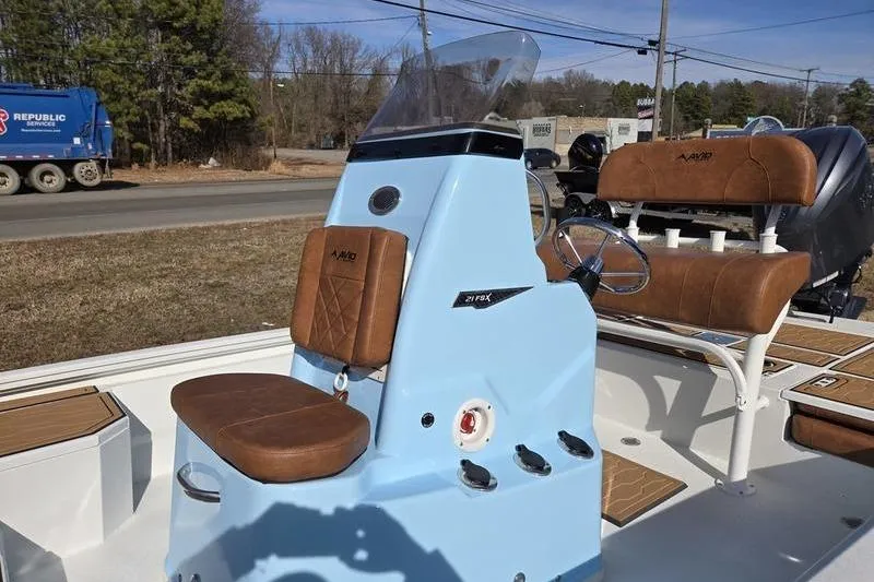 Slide: The Image of 2026 Avid 21 FSX boat with brown seating and blue console, parked outdoors. - 10