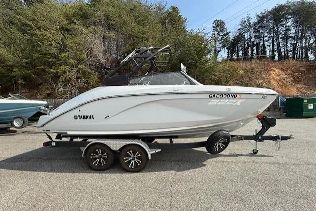 The Image of 2023 Yamaha Boats 222XE on trailer, parked outdoors with trees in the background. - 1