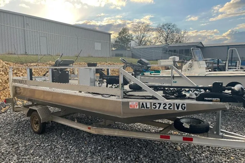 Slide: The Image of 2024 CustomBilt Pondtoon 1672 boat on trailer, parked outdoors with other boats. - 4