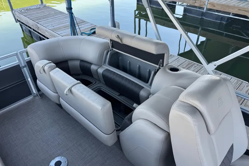 Slide: The Image of 2024 Sun Tracker Party Barge 24 DLX interior seating with storage, docked by the water. - 9
