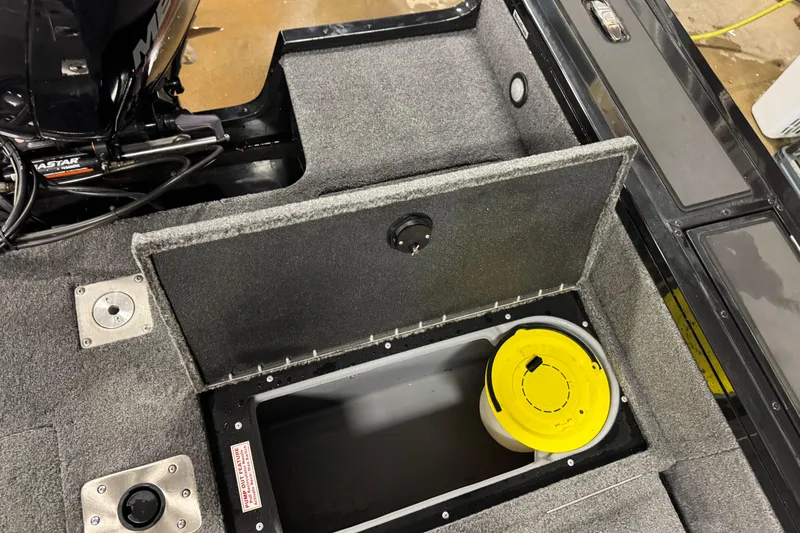 Slide: The Image of 2024 Tracker Targa V-18 Combo boat storage compartment with yellow lid and motor detail. - 14