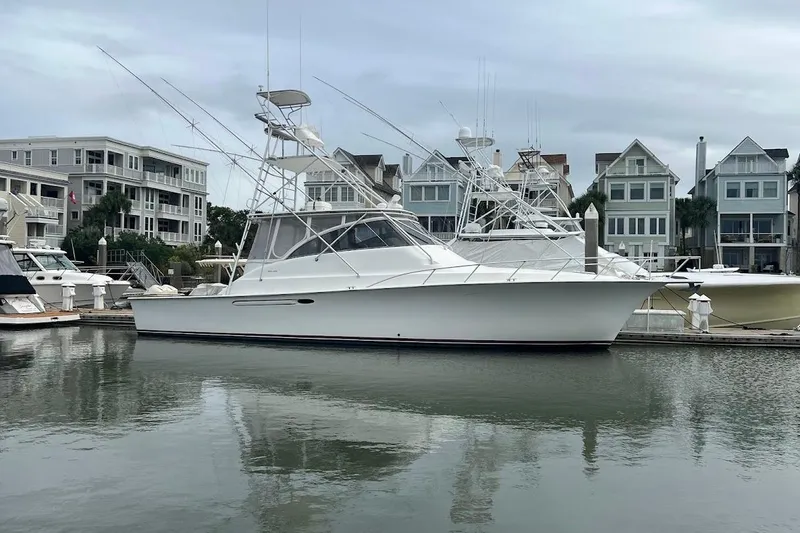 Slide: The Image of 1999 Ocean Yachts 48 Express docked at marina with waterfront homes in background. - 2
