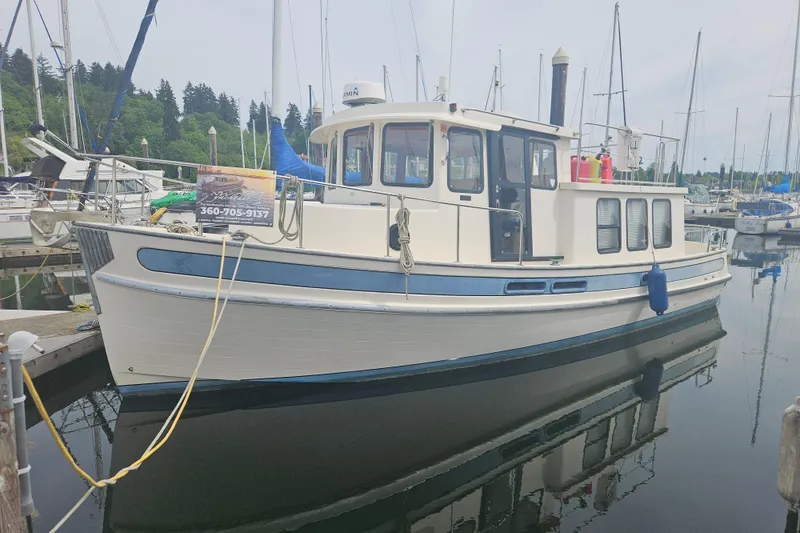 The Image of 1998 Nordic Tug 32 docked at a marina, surrounded by sailboats and calm water. - 0