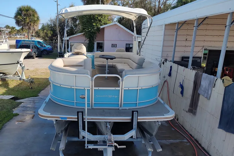 The Image of 2019 South Bay S222FCR pontoon boat on trailer, parked near a building. - 0