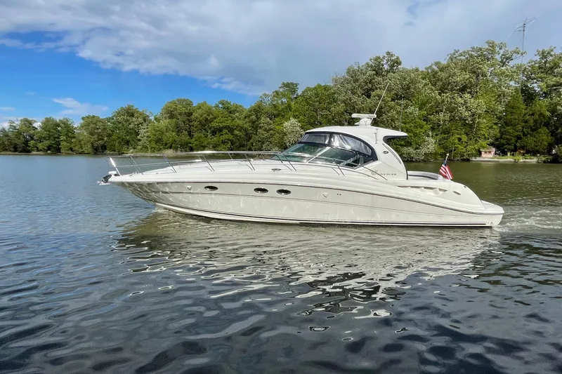 Slide: The Image of 2004 Sea Ray 420 Sundancer yacht cruising on a serene lake with lush green trees. - 2