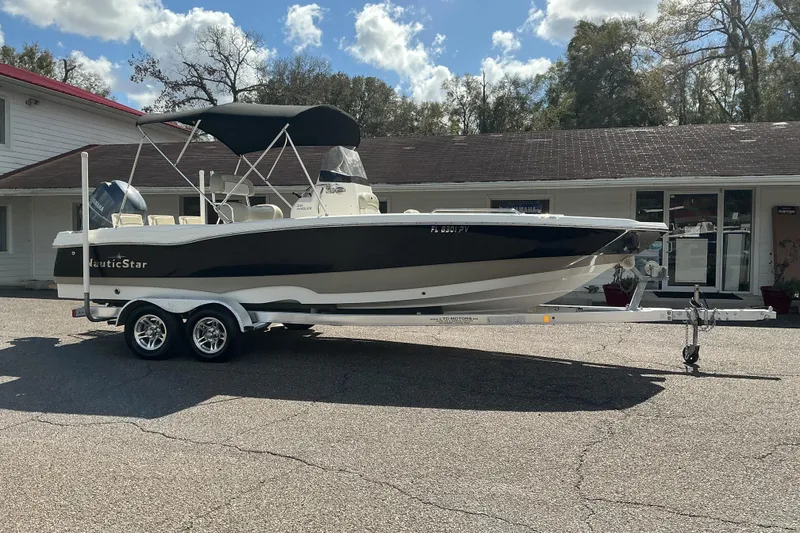 Slide: The Image of 2015 NauticStar 231 Hybrid boat on trailer, parked outdoors under a cloudy sky. - 2