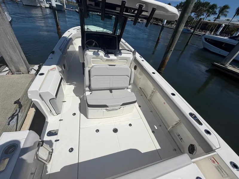 Slide: The Image of The image shows a 2026 Boston Whaler 330 Outrage boat docked. It features a spacious white deck with seating and a helm. - 23