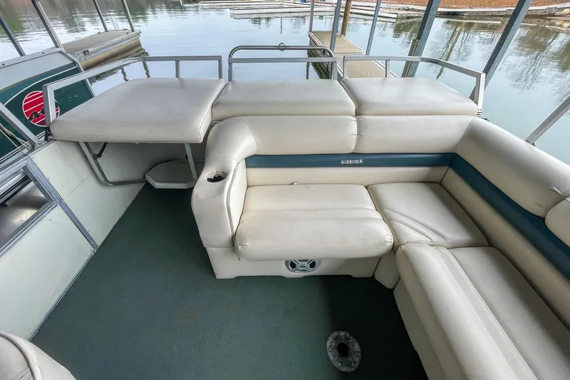 Slide: The Image of 2000 Crest 25' Pontoon interior with beige seating and table, docked by the water. - 15