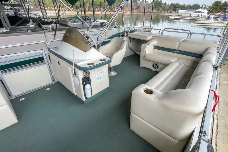 Slide: The Image of 2000 Crest 25' Pontoon boat interior with seating and steering console, docked by the water. - 9