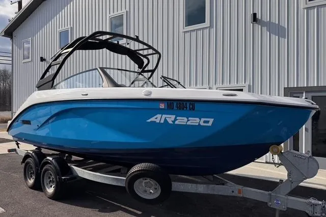 The Image of 2023 Yamaha Boats AR220 on trailer, blue hull, parked outside a building. - 0