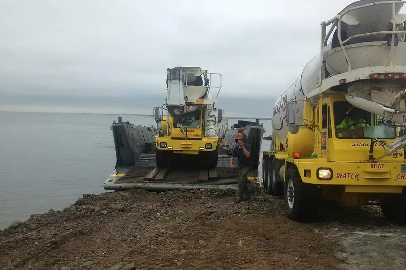 Slide: The Image of Yellow cement trucks on a 1987 Commercial LCU 8 landing craft by the shore. - 3
