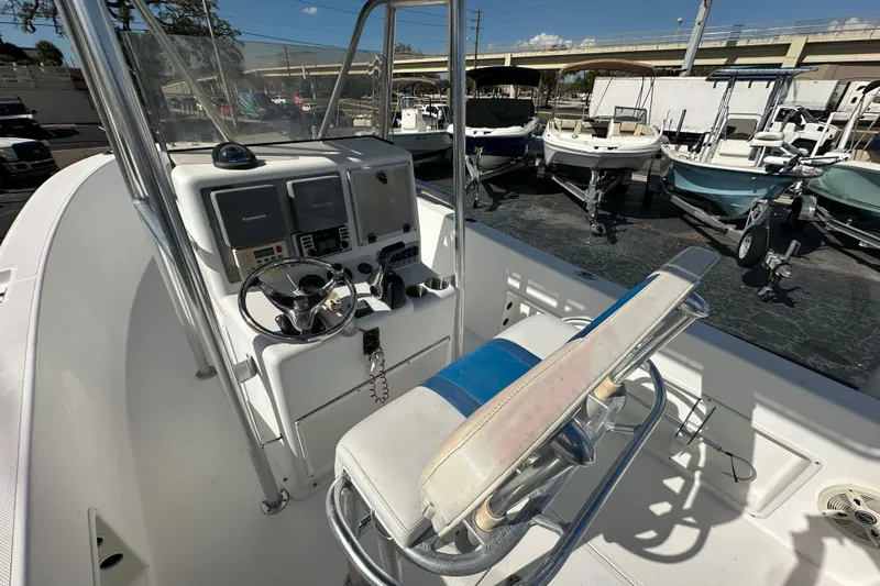 Slide: The Image of 1998 Bluewater 2150 boat cockpit with steering wheel and control panel, docked among other boats. - 15