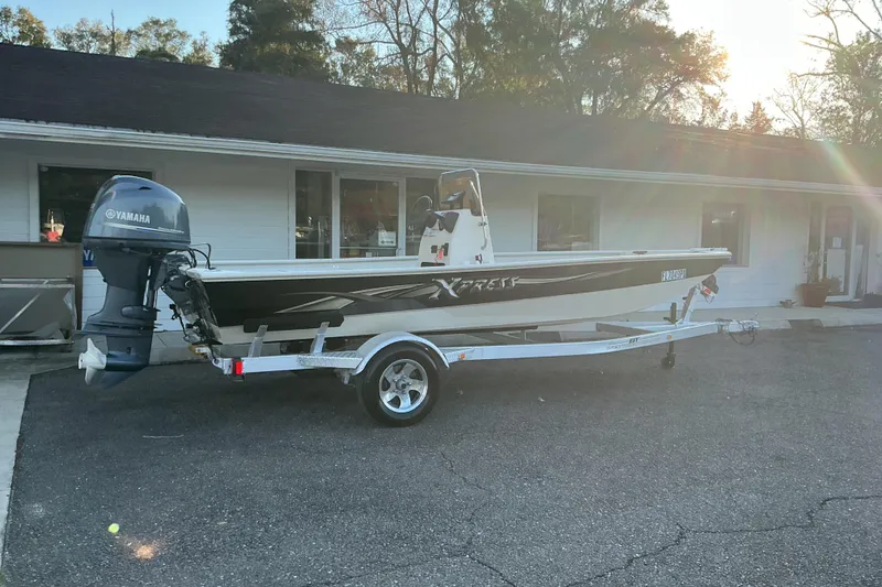 Slide: The Image of 2013 Xpress XP18CC boat with Yamaha outboard motor on a trailer, parked outside a building. - 2