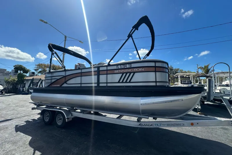 Slide: The Image of 2022 Bennington 22 L Quad Bench pontoon boat on trailer under clear blue sky. - 6