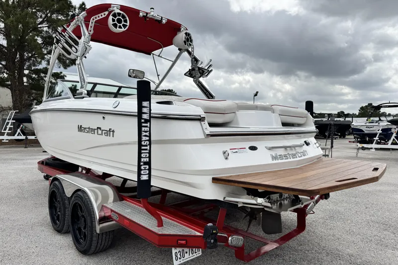 Slide: The Image of 2011 MasterCraft X25 boat on trailer with red accents, under cloudy sky. - 5