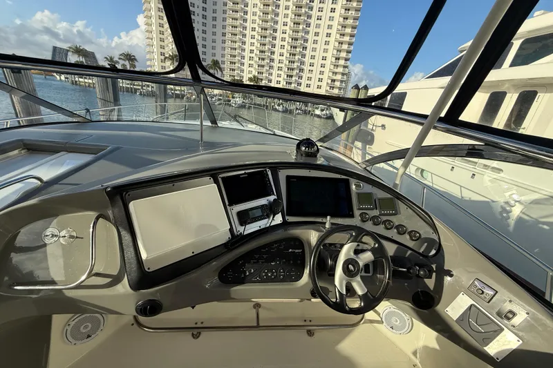 Slide: The Image of 2007 Cruisers Yachts 560 Express helm with modern navigation controls, docked near waterfront buildings. - 14