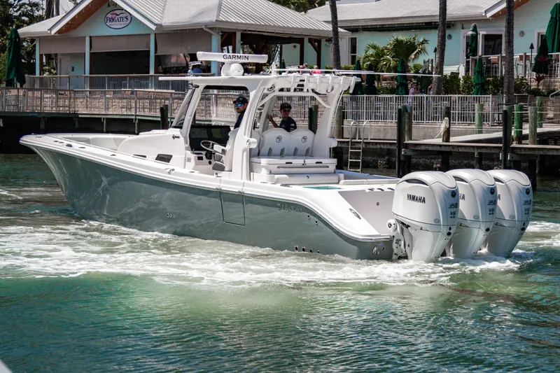 Slide: The Image of 2025 Edgewater 370CC boat with triple Yamaha engines cruising near a dock. - 6