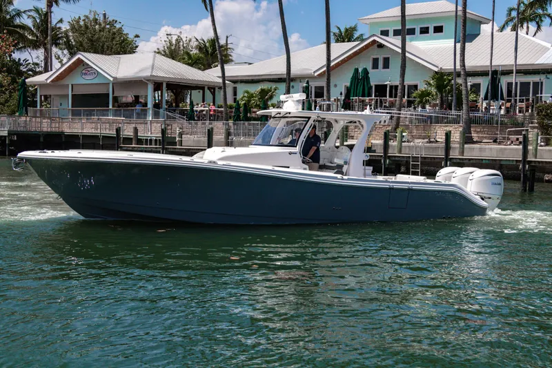 Slide: The Image of 2025 Edgewater 370CC boat cruising near a waterfront restaurant with palm trees. - 2