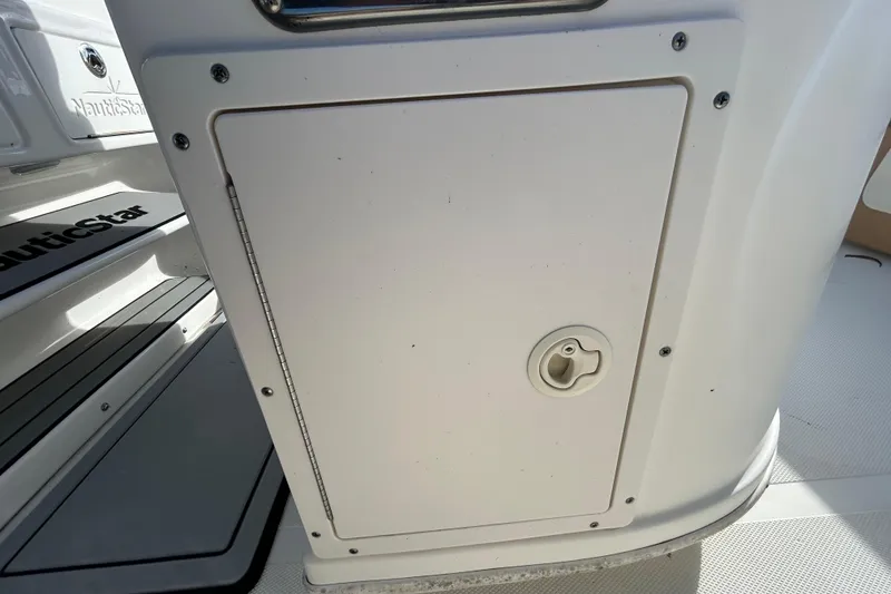 Slide: The Image of 2016 NauticStar 25 XS boat storage compartment with handle and branding. - 64