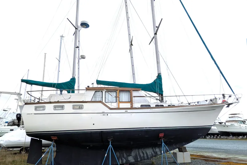 Slide: The Image of 1985 Siltala Nauticat 44 sailboat on stands, with green covers, in a boatyard. - 2