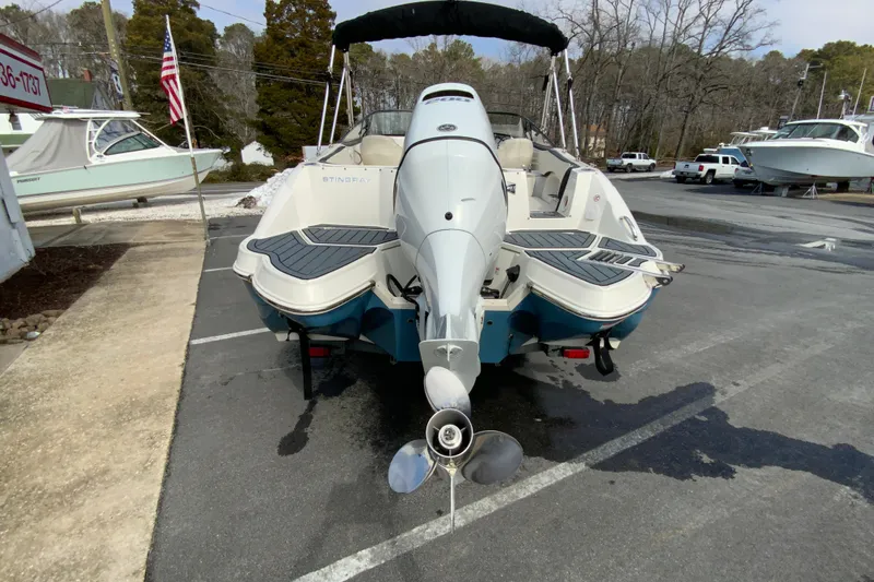 Slide: The Image of 2023 Stingray 231 DC boat, rear view, parked outdoors with American flag nearby. - 9