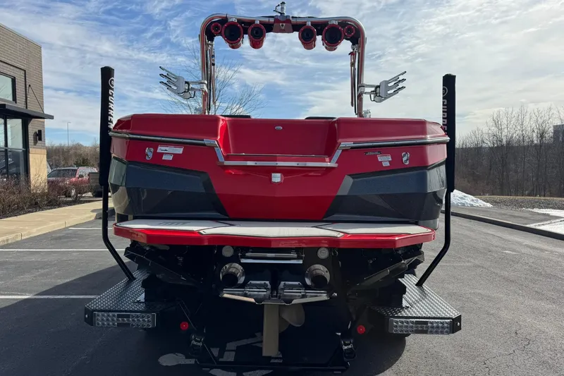 Slide: The Image of 2020 MasterCraft XStar boat, red and black, parked outdoors on a sunny day. - 7
