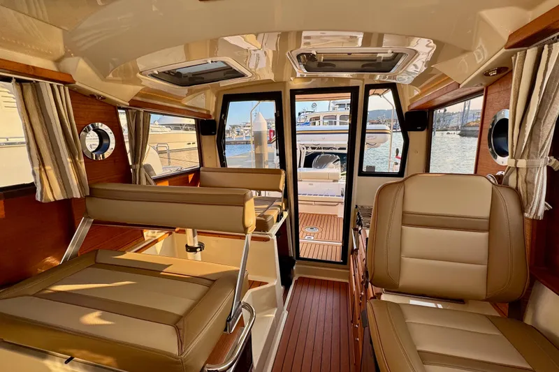 Slide: The Image of 2024 Ranger Tugs R-27 interior with leather seating and wood accents, docked at marina. - 10