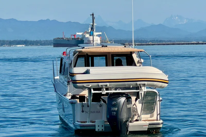 Slide: The Image of 2024 Ranger Tugs R-27 boat cruising on calm waters with mountains in the background. - 2