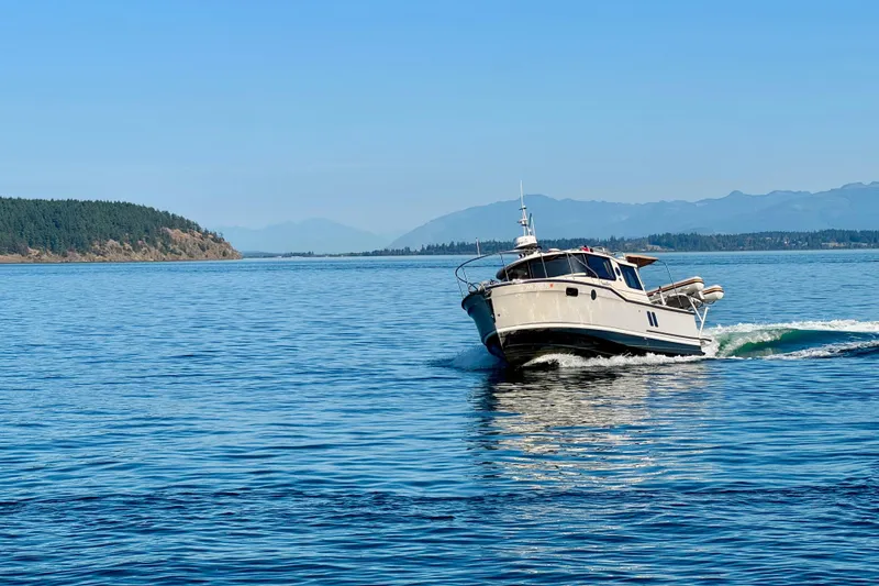 Slide: The Image of 2024 Ranger Tugs R-27 cruising on a serene blue lake with distant forested hills. - 33