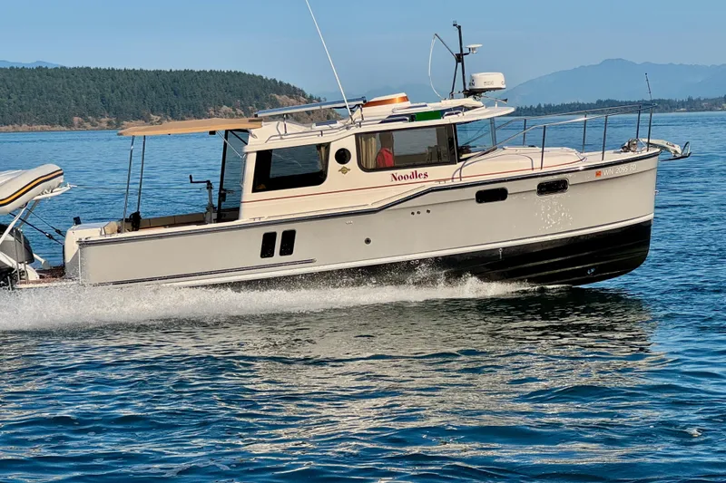Slide: The Image of 2024 Ranger Tugs R-27 cruising on a scenic lake with forested hills in the background. - 35