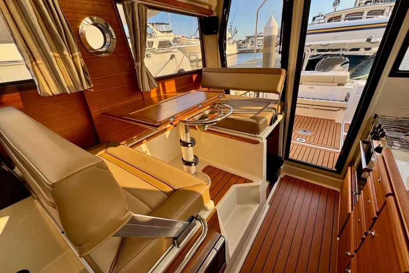 Slide: The Image of 2024 Ranger Tugs R-27 interior with wood accents and seating, docked at marina. - 6