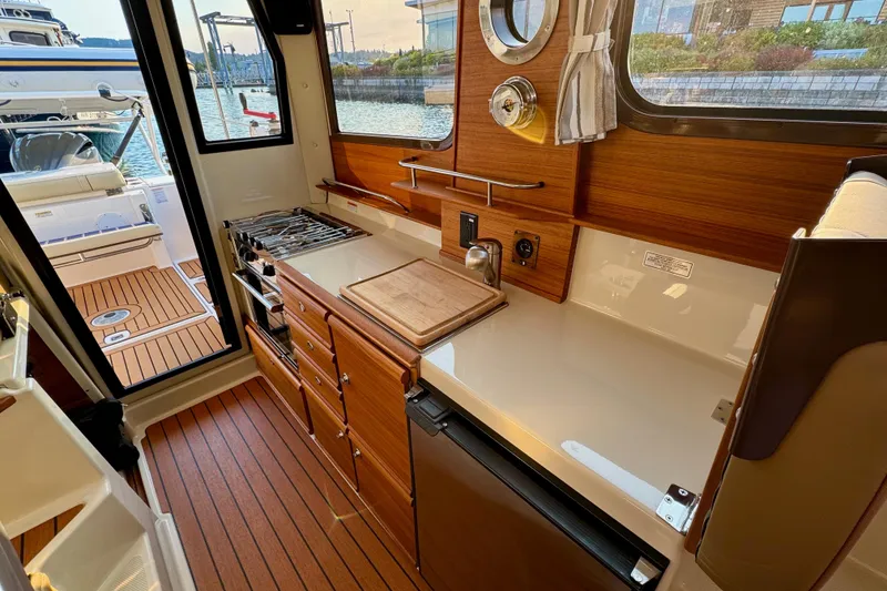 Slide: The Image of 2024 Ranger Tugs R-27 interior kitchen with wood cabinetry and modern appliances. - 9