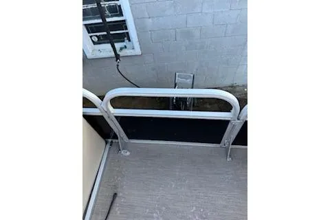 Slide: The Image of 2023 Sun Tracker Fishin' Barge 20 DLX deck with railing, near a brick wall. - 11