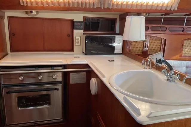 Slide: The Image of 1990 Ericson 34 yacht kitchen with stove, sink, and microwave in wooden interior. - 12